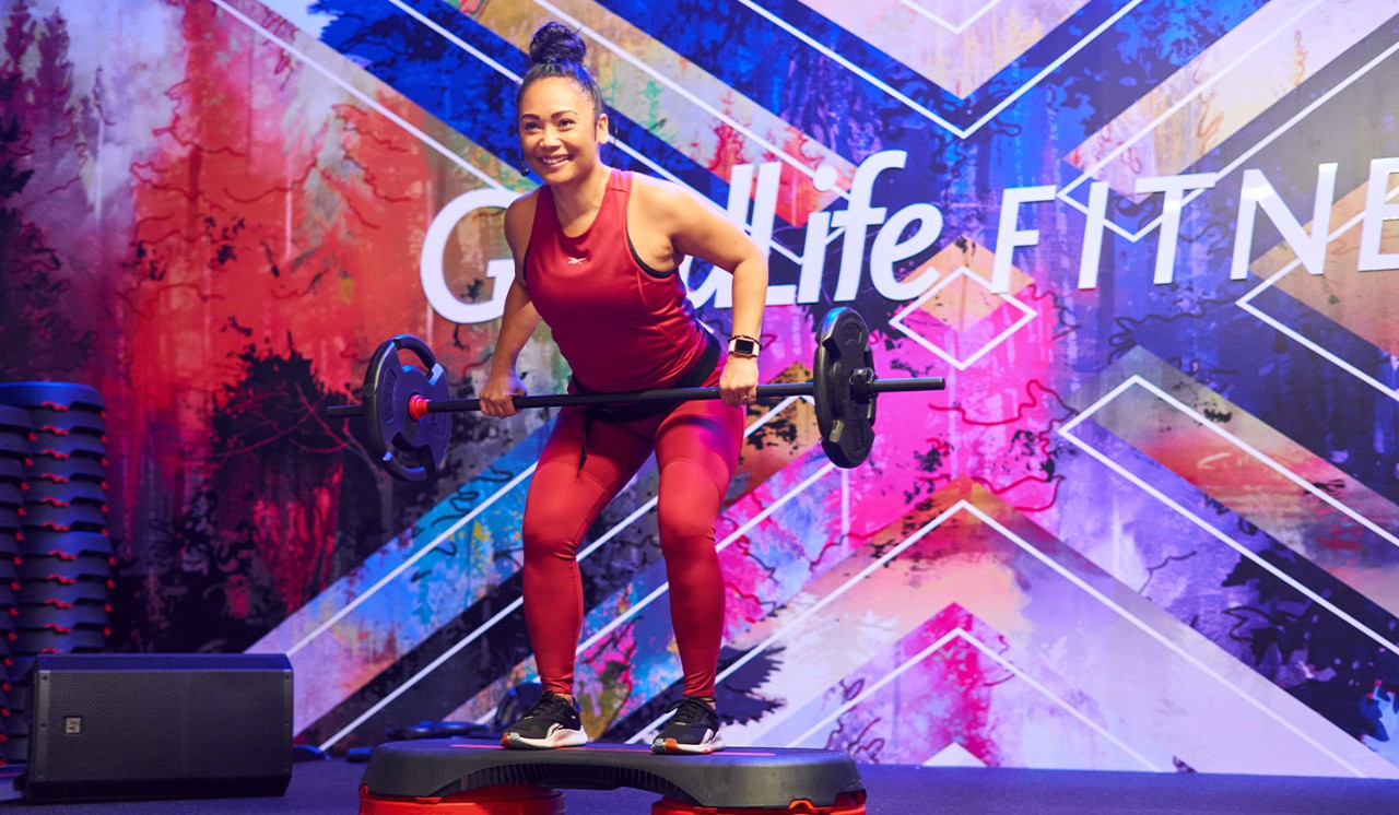 A GoodLife Fitness Group Fitness instructor on a stage leads a strength class.