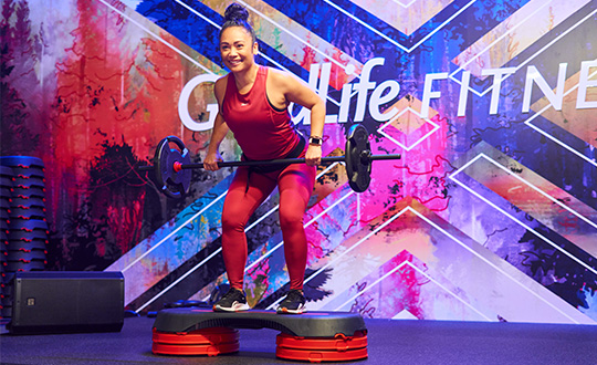Woman in mint green tank top doing a barbell squat in weight area