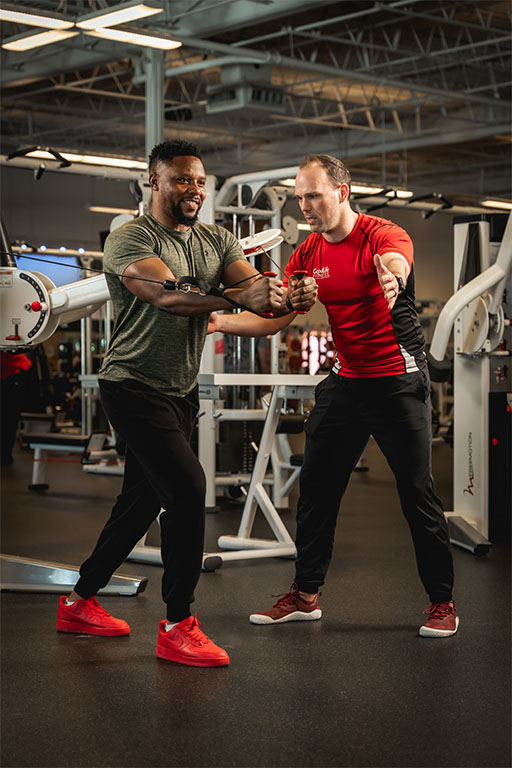 A GoodLife Fitness Personal Trainer spotting a member who is using a weight machine.
