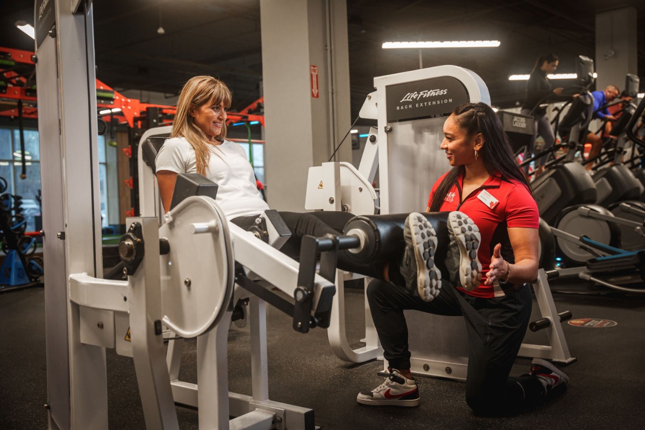 GoodLife Personal Trainer observes woman in black shirt doing shoulder press